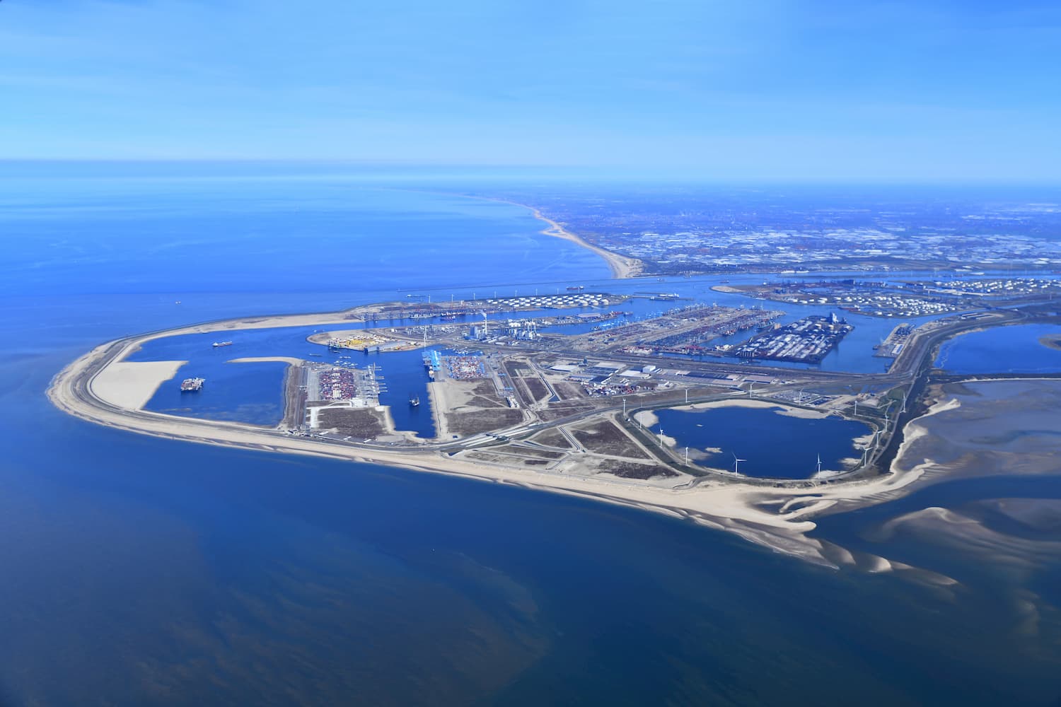 Luchtfoto van een havengebied met terminals, tanks en windturbines