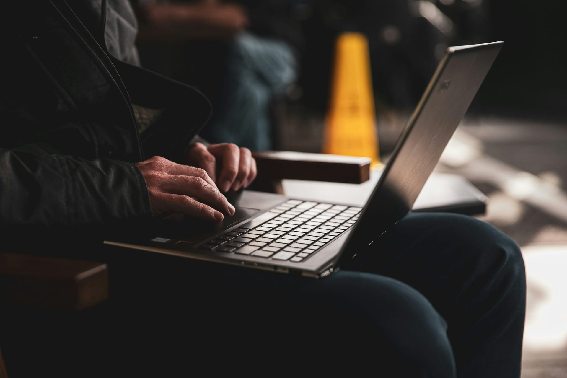 Handen typen op een laptop, met een pion van een werkterrein op de achtergrond