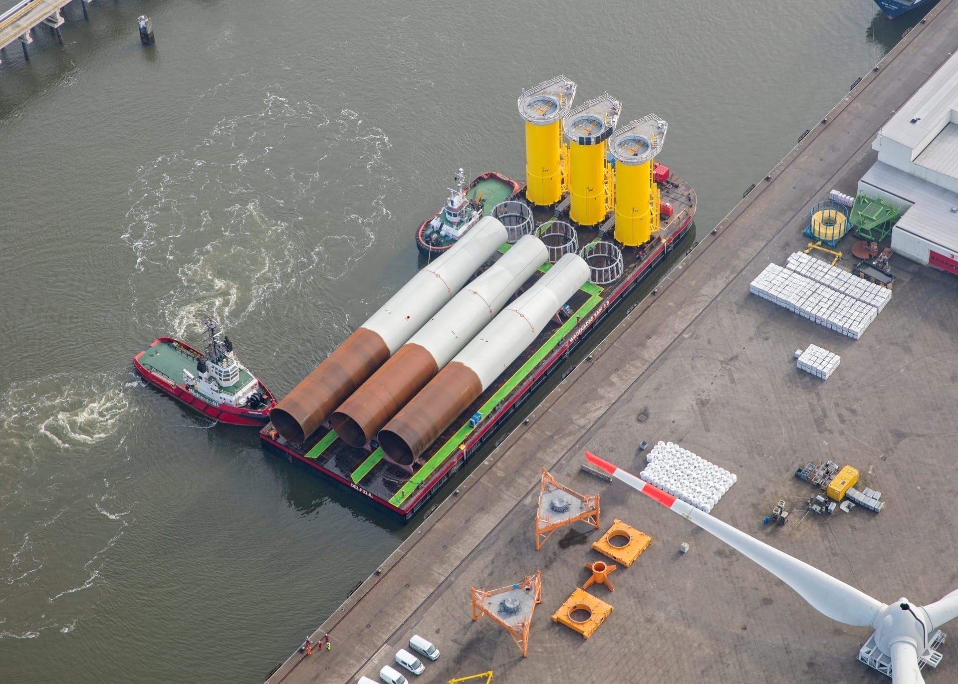 Identieke monopiles en transition pieces klaar op een ponton in de haven
