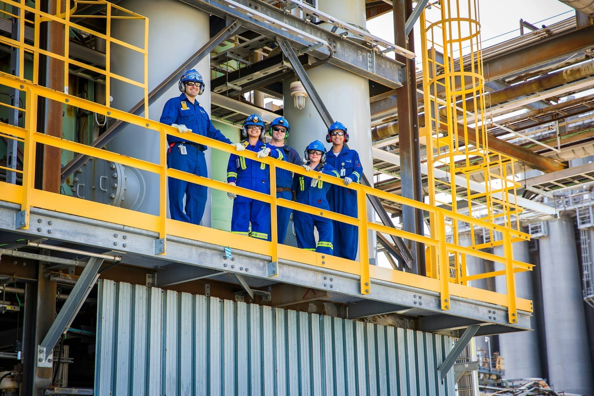 Ploeg medewerkers in overall en met gehoorbescherming op een bordes van een installatie