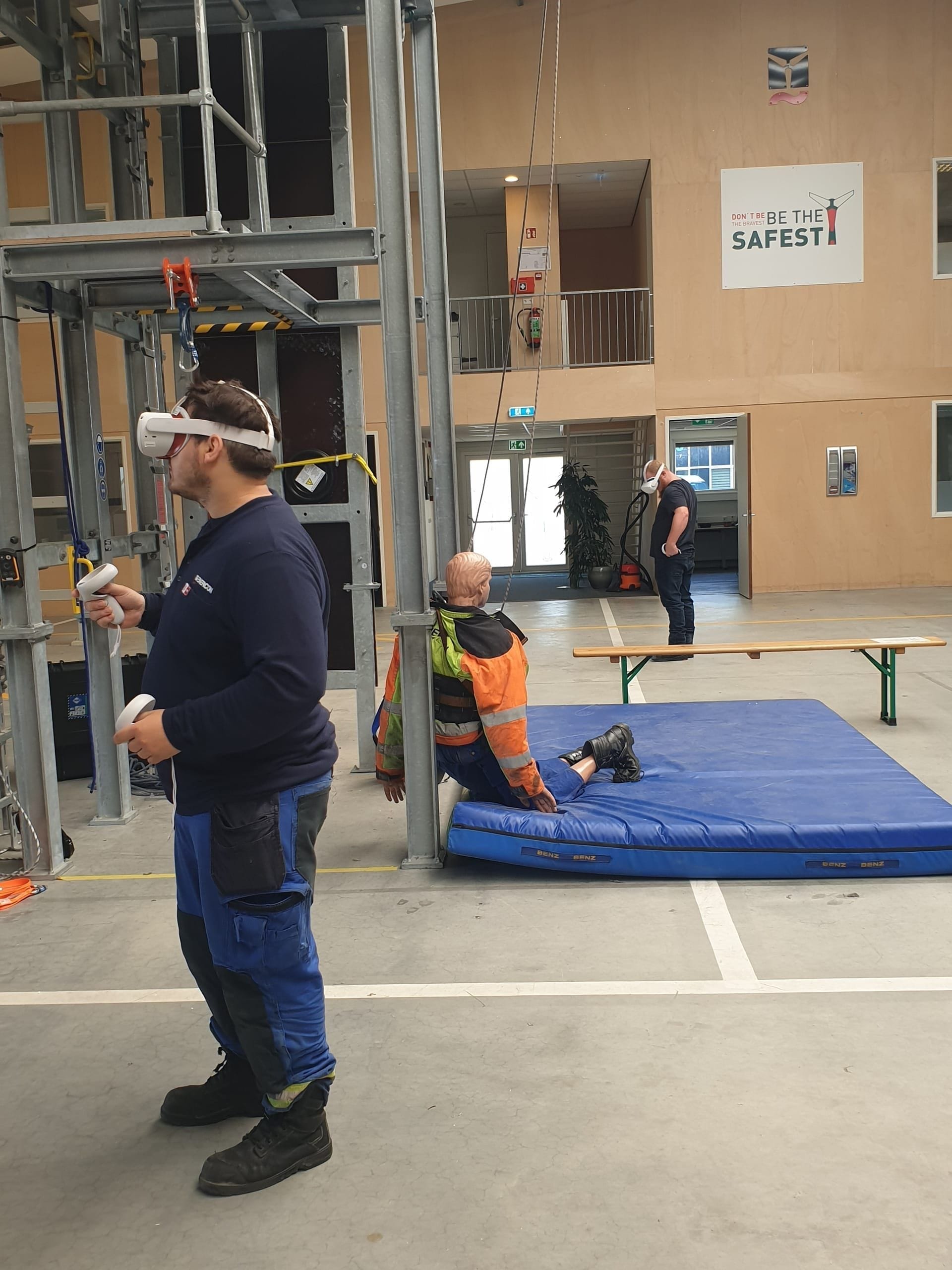 Monteur oefent met een VR-bril naast een oefenpop op een valmat in een werkhal
